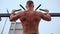 Athletic Man Pumps Up Muscles Doing Pull-Ups Open Sports Ground with Bare Torso