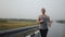 Athletic man runs outdoor on road in steppe doing workout during rain, front view. Man runs along highway during