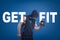 Athletic man in sleeveless hoody posing half-turn with dumbell in one hand on blue background with title GET FIT.