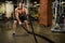 Athletic muscular man engaged with a thick rope with a bare torso in the gym.