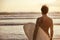 Athletic surfer stands with surfboard at sunset beach