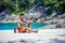 Athletic tattooed guy reading book on the sand at the beach