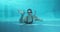 Athletic teenager girl swimmer underwater in blue outdoor pool looking at camera, waving his hand, hi hello gesture