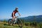 Athletic tourist cyclist in helmet, sunglasses and full equipment riding bike down grassy hill