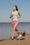 athletic woman and beagle dog run along sandy beach on seashore in morning. outdoor