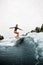 Athletic woman in black wetsuit effectively jumps on surf board on wave
