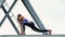 Athletic woman in a Blue top and striped leggens performs strength exercises.She stands on the metal beam of a freight