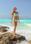 Athletic woman in cyan blue bikini standing on rocks with turquoise sea behind her