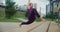 Athletic woman does twine on the bench in a public yard, stretching exercises in the urban environment, yoga class