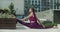 Athletic woman does twine in a public yard, stretching in the urban environment, yoga class outdoors in slow motion