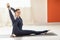 Athletic woman practicing yoga, performs yantrasana exercise, compass pose, trains in sports overalls sitting on a mat in the room