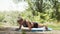 Athletic woman shakes her abs in nature. A young woman holds plank while pumping her ABS muscles on Mat in the fresh air