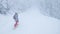 Athletic woman snowboards along a groomed slope leading through foggy forest.