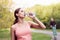 Athletic woman standing running track in summer park drink water after running exercises