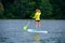 Athletic young girl-surfer riding on the stand-up paddle board in the clear waters of the on the background of green trees