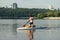 Athletic young man actively spends time on the water, swims on a sup board, paddles and looks away. Surfing on the lake on a sup