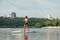 Athletic young man with a naked torso floats on the river on a sup board, rowing with an oar on the background of a beautiful