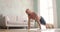 Athletic young shirtless man in shorts doing push-ups in living room at home.