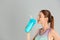 Athletic young woman drinking protein shake on light grey background