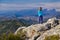 Athletic young woman standing on the rocky top of the mountain against the blue sky