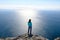 Athletic young woman standing on the rocky top of the mountain against the blue of sky and sea