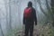 An atmospheric concept. Of a hiker with a rucksack, back to camera. standing in a forest on a cold, foggy autumn day. UK