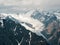 Atmospheric landscape with fuzzy silhouettes of sharp rocks and snowy mountaintop in low clouds during rain. Dramatic view to