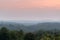 Atmospheric landscape scene of lush forest layers in mist during autumn dusk in countryside