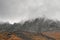 Atmospheric misty landscape with fuzzy silhouettes of sharp rocks in low clouds during rain. Dramatic view to large mountains