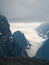 Atmospheric vertical landscape with fuzzy silhouettes of sharp rocks and snowy mountaintop in low clouds during rain. Dramatic