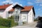 Attached newly built small suburban family house with closed front porch and small balcony surrounded with stone tiles covered