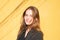 Attarctive smiling brunette girl with blue eyes in black cloak, yellow wall on the background