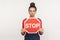 Attention, prohibited way! Portrait of serious girl with hair bun holding octagonal Stop symbol, showing red traffic sign