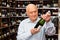 Attentive elderly man chooses champagne in a liquor store
