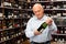 Attentive elderly man chooses champagne in a liquor store