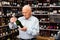 Attentive elderly man chooses champagne in a liquor store