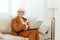 attentive elderly woman in a classic suit in a bright room on the sofa and working on a laptop remotely