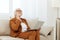 attentive elderly woman in a classic suit in a bright room on the sofa and working on a laptop remotely