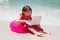 Attentive little girl sitting on beach with laptop