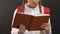 Attentive schoolgirl with rucksack reading book against blackboard, homework