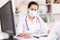 Attentively young female doctor in protective mask working at laptop in office