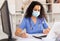 Attentively young female doctor in protective mask working at laptop in office