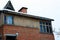 Attic brown house of brick and wooden planks with windows and icicles on the roof