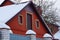 Attic of a red country barn with a door and windows and white snow on the roof behind the fence