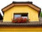 Attic window of yellow stone house decorated with red geranium