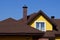 Attic of a yellow house with a window and a brown tiled roof against the sky