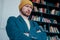 Attractive adult bearded angry man hipster in yellow hat looks at camera and furrowed his brows on books wall background