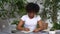 Attractive African-American young woman sitting at desk using laptop, listening audio course through headphones, making