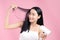 Attractive Asian woman usinf hair dryer on pink background