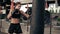 Attractive athletic female boxer in gloves exercising with a bag. Workout outside. Female boxer training. Self defence